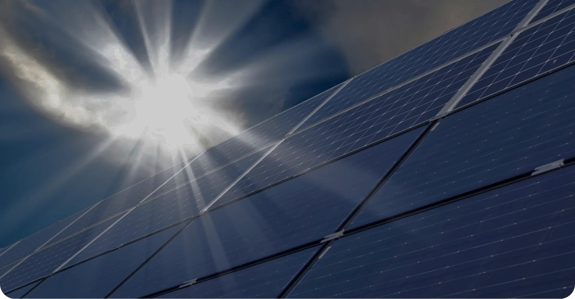 Sonnenstrahlen scheinen auf eine Fläche von Solarpaneelen vor bewölktem Himmel.
